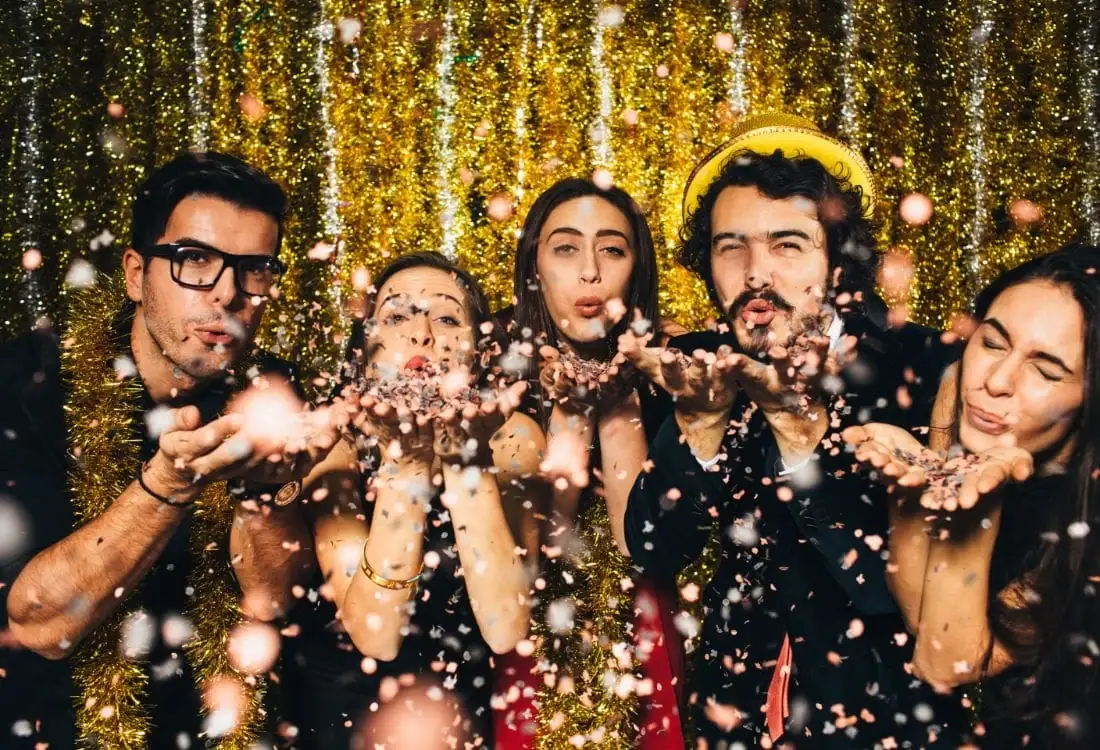 A group of five friends blowing glitter into the air as they celebrate the new year at a party that is alcohol free.